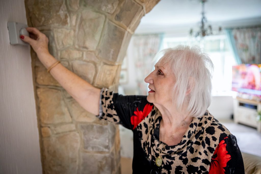 A woman adjusts her thermostat after making affordable renovations to her HVAC system.